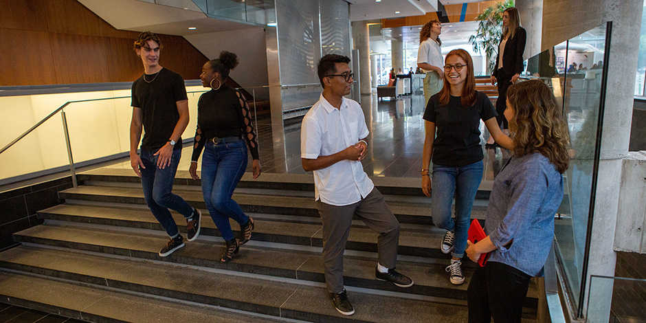 A group of students chat in the atrium of the John Molson Building while other student walk by them